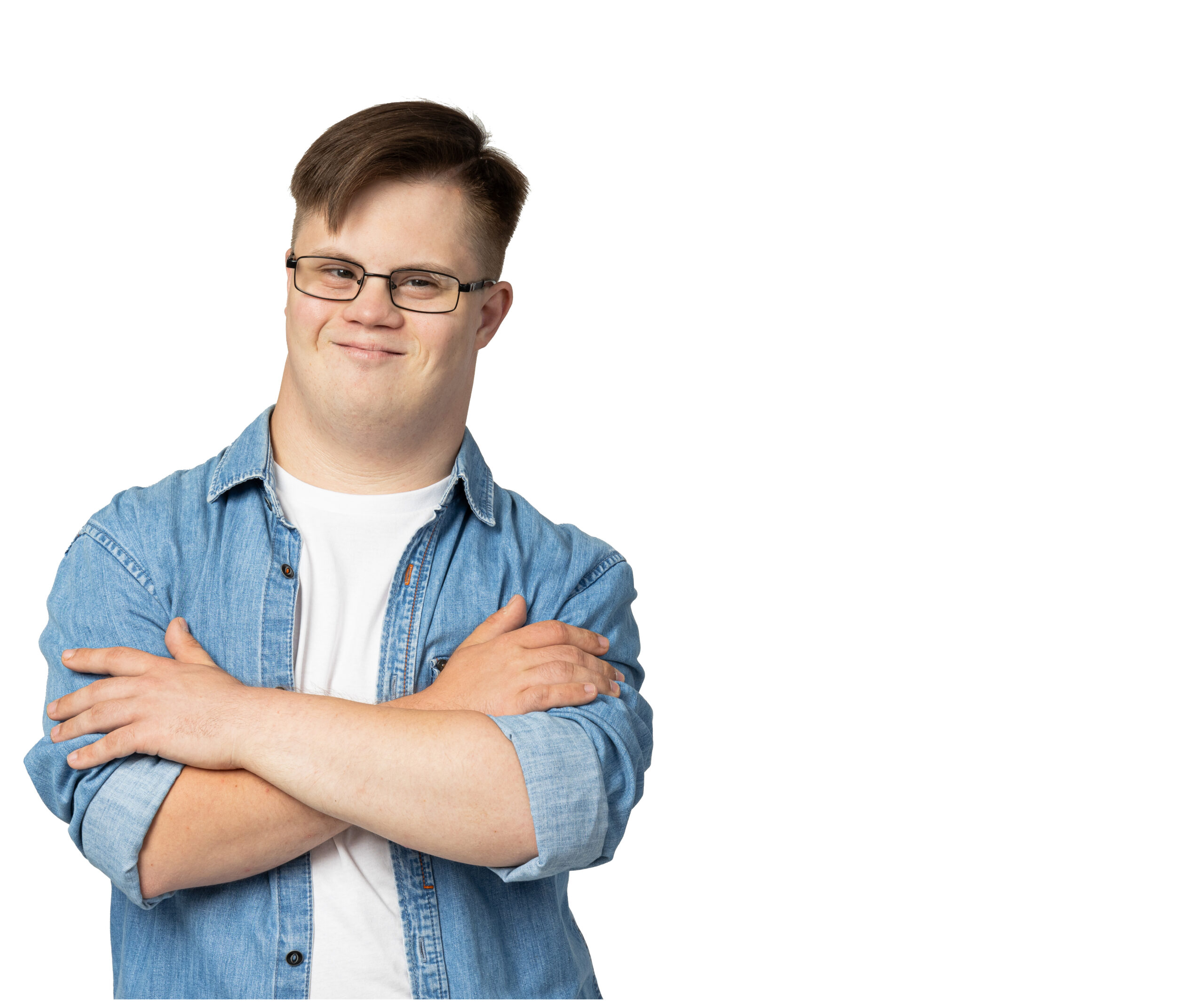 Berufliche Teilhabe im Fokus Ein junger Mann mit Beeinträchtigung steht vor weissem Hintergrund, trägt Jeanshemd und Brille und lächelt mit verschränkten Armen in die Kamera.